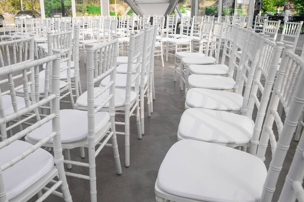 Cadeiras brancas vazias para convidados em um banquete ou casamento em uma área de verão ao ar livre estão em uma fileira
 - Foto, Imagem