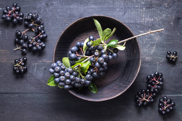 Freshly picked homegrown aronia berries in wooden bowl - Foto, afbeelding