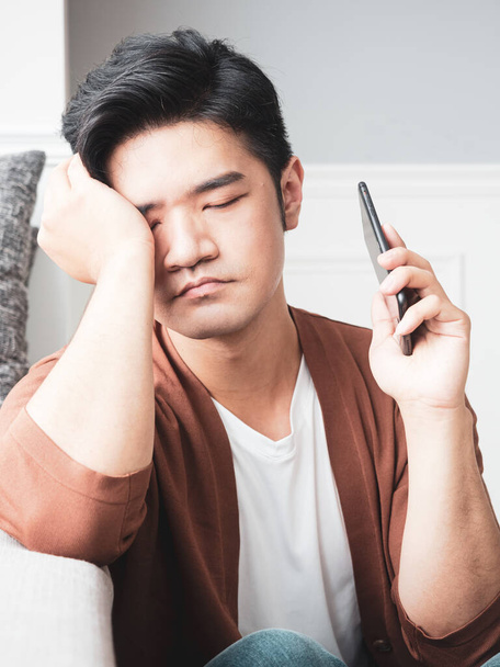 Asiatique jeune homme frottant ses yeux fatigués son smartphone. - Photo, image