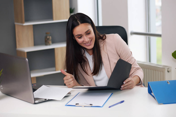 Happy businesswoman with raised so hand gesture reading letter on desk in front of laptop. The businessman is satisfied with the good news from the correspondence. - Fotó, kép