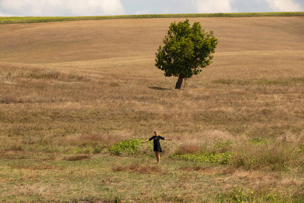 una niña entra en un campo en Ucrania en agosto y hay un árbol cerca - Foto, Imagen