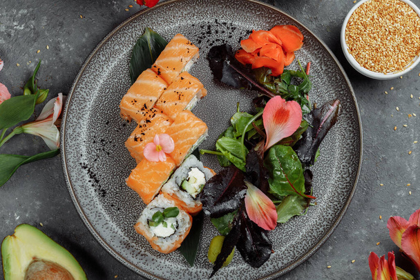 Deliziosi involtini di sushi fresco con salmone e formaggio filadelfia su piatto grigio su sfondo pietra scura. Pesce tradizionale giapponese, concetto di cibo sano. - Foto, immagini