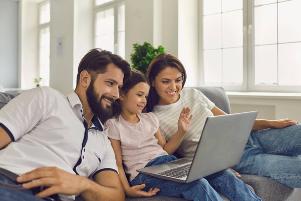 Parents and child online. Beautiful family uses laptop watching video at home. - Foto, Imagem