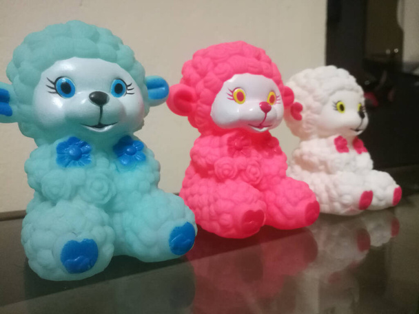 線の上に3体の異なる色の羊の人形が置かれています。羊の人形は小さく、白、赤、青の色をしています。. - 写真・画像