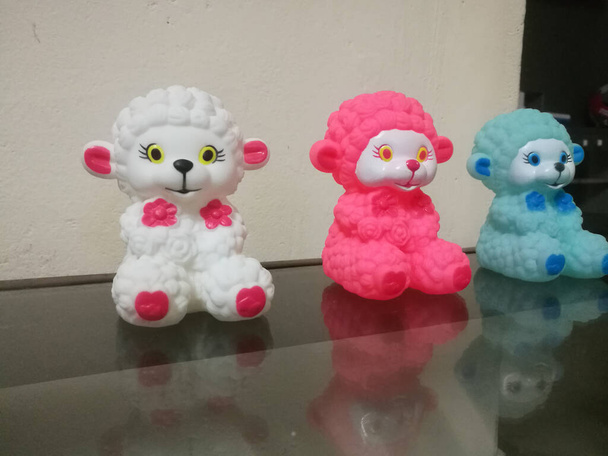 Three sheep dolls of different colors placed in a line.The sheep dolls are small and they have white, red, and blue colors.They are cute and beautiful.Their reflection are made using glass in the front. - Фото, изображение