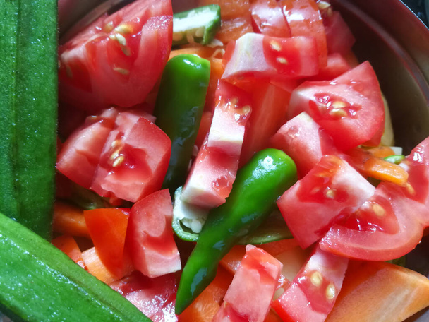 Chopped Tomatoes and green chilli in a plate.The tomatoes have red color and water runs out from the tomatoes.Two lady's finger are placed near to the tomato. - Fotoğraf, Görsel