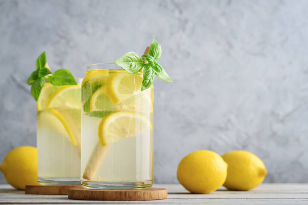 Lemonade with lemon and basil, cold refreshing drink in glasses on grey background - Photo, image