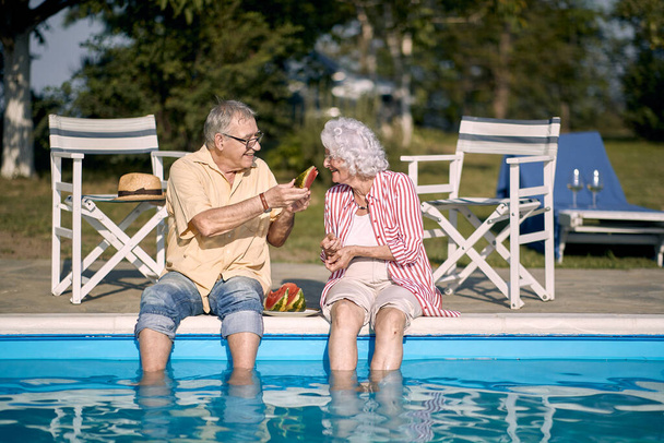 Romantic happy elderly couple  enjoy on summer holiday near swimming pool and  eating watermelon. - Фото, зображення