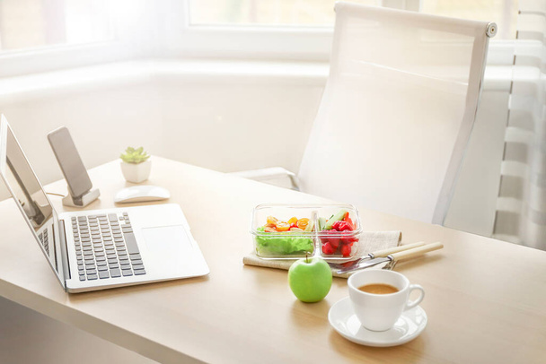 Healthy business lunch in office workplace. Vegetable and chicken salad in lunch box and coffee in white cup on wooden desk near laptop. - Photo, Image