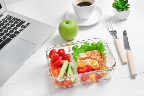 Healthy business lunch in office workplace. Vegetable and chicken salad in lunch box and cup of coffee on white wooden desk near laptop. - Fotó, kép