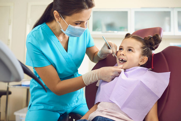 Mała dziewczynka u dentysty pediatry z maską i rękawiczkami obsługa dziecięcej pielęgnacji zębów w klinice stomatologicznej. - Zdjęcie, obraz