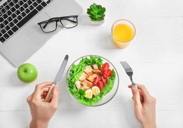 Healthy business lunch in office workplace. Businessman having vegetable and chicken salad in bowl on white wooden desk near laptop. Top view. - Foto, immagini