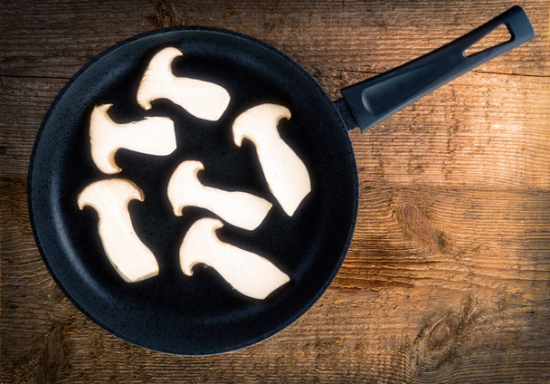 Τηγάνι τηγανίσματος με μανιτάρια τρομπέτας σε φέτες σε φόντο από ξύλο. - Φωτογραφία, εικόνα