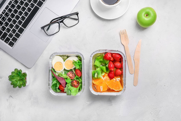 Gezond zakenlunchen op kantoor. Bovenaanzicht van groente- en kipsalade in lunchbox, verse groene appel en kop koffie op wit bureau bij laptop en bril. - Foto, afbeelding