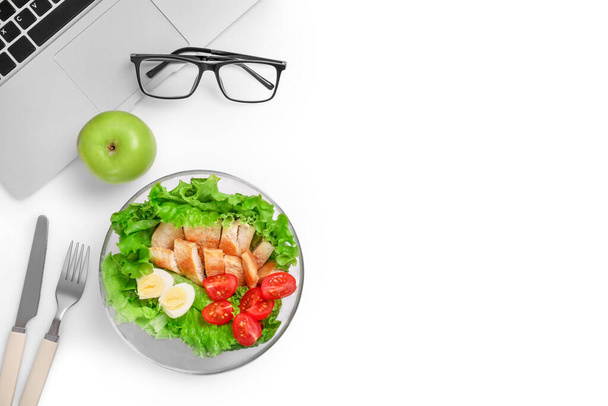 Healthy business lunch in office workplace. Top view of vegetable and chicken salad in bowl and fresh green apple on white desk near laptop and glasses. Copy space. - Foto, Bild