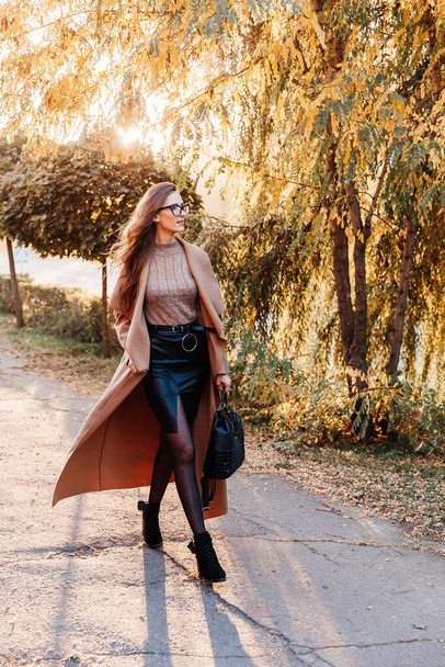 コートに黒いスカートに秋のジャケットを着た美しい女の子が帽子の中を歩く - 写真・画像