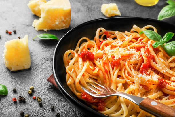 Italienische Pasta mit Tomaten, Käse-Parmesan und Basilikum auf schwarzem Teller auf dunklem Hintergrund. - Foto, Bild