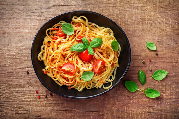 Italialaista pastaa tomaattien, juuston parmezanin ja basilikan kanssa mustalla lautasella puupohjalla. Yläkuva. - Valokuva, kuva