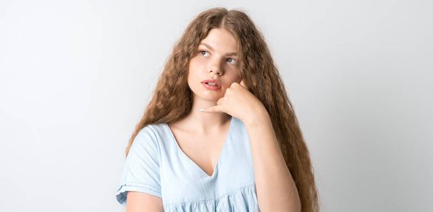 Фото Pensive European young woman with curly long hair, looking up having pensive expression. Изолированный на белом фоне. - Фото, изображение