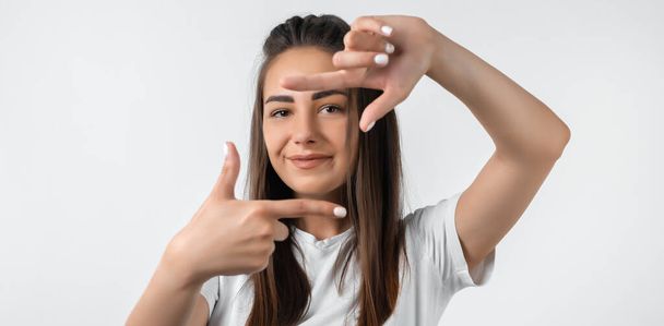 Portrait positive of young woman with long chestnut hair with cheerful expression. Gesturing finger frame. Beautiful young woman looking at camera and gesturing finger frame - Fotó, kép