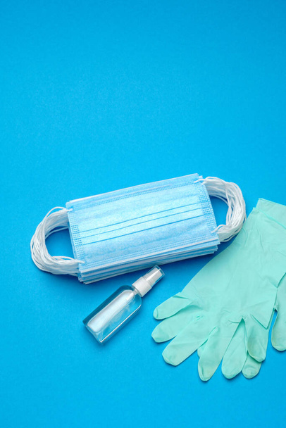 Stack of Disposable blue medical face masks, rubber latex gloves and alcohol hand sanitizer antiseptic on blue background - Foto, Bild