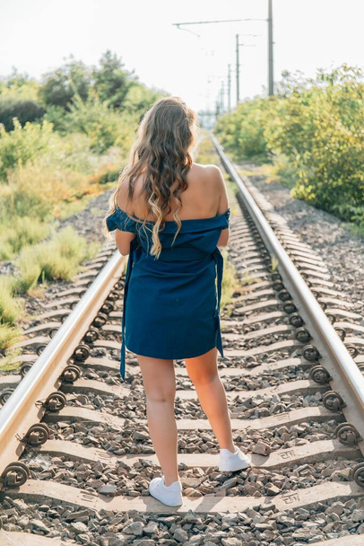 鉄道の上を歩く青いドレスを着た美しく魅力的な女性。背景画像. - 写真・画像