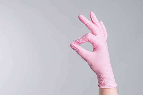 A közelkép orvos kezét rózsaszín gumikesztyűben mutatja OK jel szürke háttér, orvosi koncepció - Fotó, kép