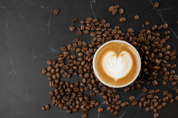 Tasse heißen Latte-Kaffee mit schönen Milchschaum Latte Art Textur mit Kaffeebohnen auf schwarzem Marmor Hintergrund. Overhead-Ansicht, Kopierraum. Werbung für die Cafékarte. Café-Speisekarte. - Foto, Bild