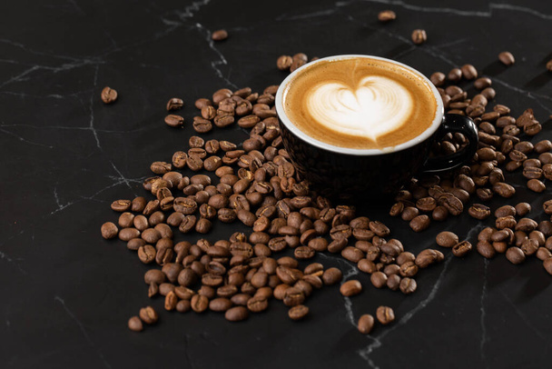 Ένα φλιτζάνι ζεστό καφέ latte με όμορφο αφρό γάλακτος latte art υφή με κόκκους καφέ σε μαύρο μάρμαρο φόντο. Εναέρια άποψη, αντιγραφή χώρου. Διαφήμιση για το μενού καφέ. Μενού καφετέριας. - Φωτογραφία, εικόνα