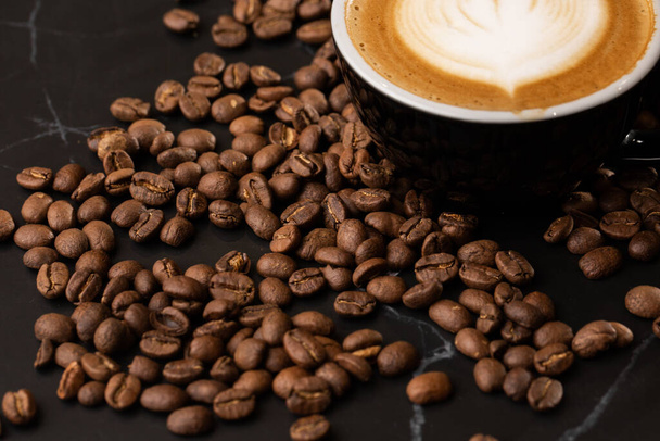 Kopje warme latte koffie met mooie melk schuim latte art textuur met koffieboon op zwarte marmeren achtergrond. Bovenaanzicht, kopieerruimte. Reclame voor cafe menu. Koffieshop menu. - Foto, afbeelding