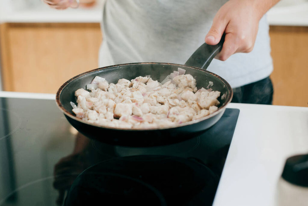 Persona arrostimento cipolla e filetto di pollo sul fornello elettrico sulla moderna cucina bianca. Processo di fare la pizza a casa, ingredienti da vicino. Concetto di cucina domestica - Foto, immagini