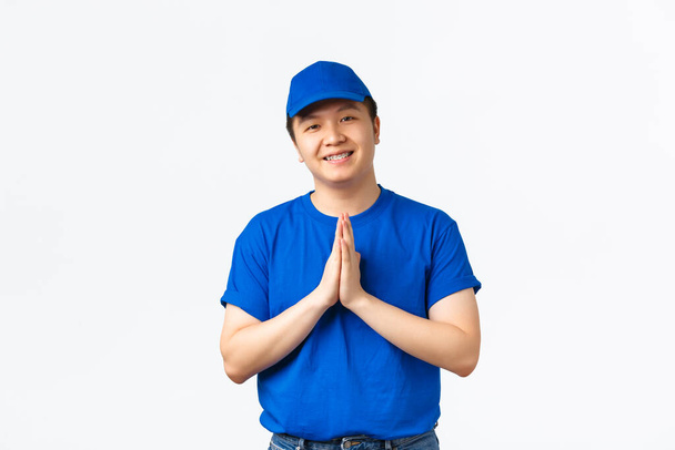Dost canlısı görünümlü Asyalı teslimatçı mavi üniformalı, el ele tutuşup, teşekkür etmek, değer ve değer vermek için el ele tutuşuyor. Kurye mutlu ve minnettar görünüyor. - Fotoğraf, Görsel