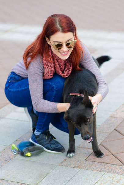 Mooie gelukkige jonge vrouw met schattige zwarte hond veel plezier op straat. Concept over vriendschap tussen dieren en mensen. - Foto, afbeelding