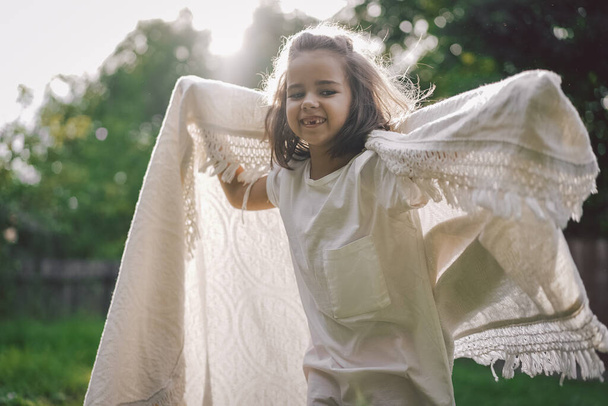 Счастливый ребенок. Забавная девушка играет с одеялом. Улыбающаяся девочка. Веселый ребенок на природе - Фото, изображение