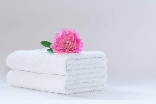 Two white neatly folded terry towels with a rose flower on a light background - 写真・画像