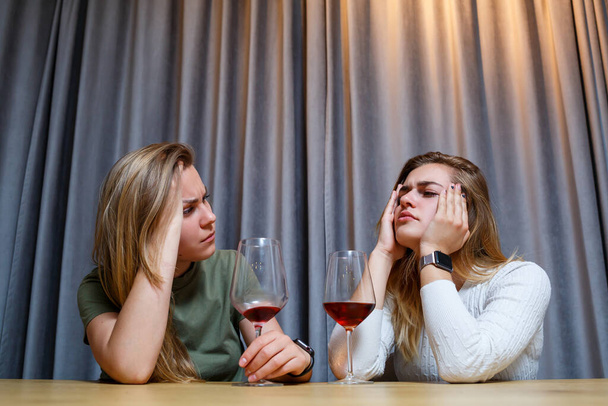 Μια γυναίκα παρηγορεί έναν καταθλιπτικό φίλο που χρειάζεται βοήθεια. Κατάθλιψη με αλκοόλ. αναστατωμένη νεαρή κοπέλα με δυστυχισμένο πρόσωπο κρατώντας ένα ποτήρι κρασί κοιτάζοντας την καλύτερη αδερφή της - Φωτογραφία, εικόνα