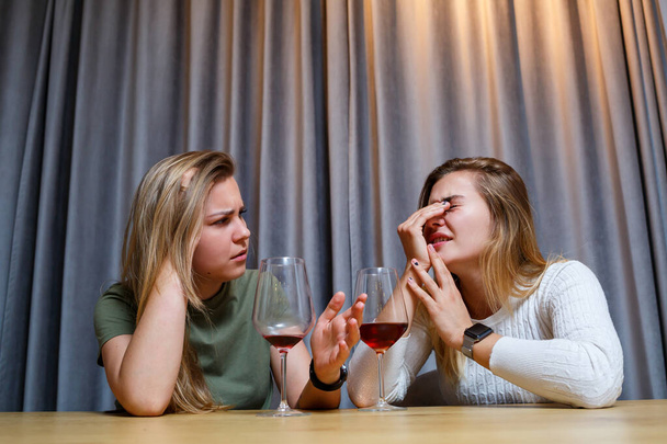 A woman consoles a sad depressed friend who needs help. Depression with alcohol concept. upset young girl with unhappy face holding a glass of wine looking at her best sister - Foto, imagen