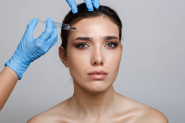 Retrato de una mujer con piel limpia sobre un fondo gris. Inserción de agujas para mesoterapia. Arrugas suavizantes - Foto, imagen