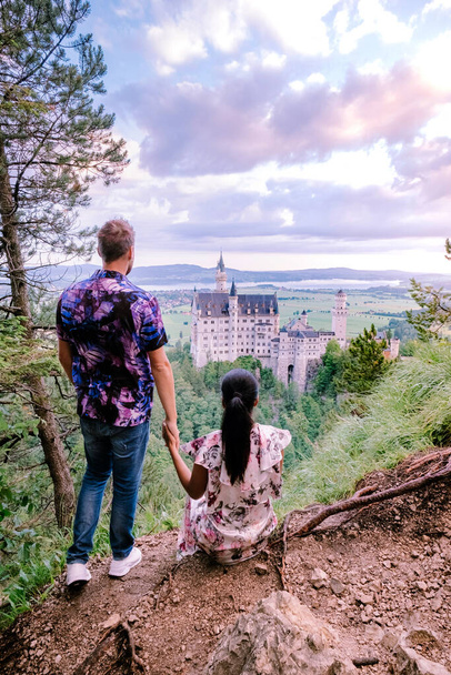 İki erkek ve kadın Neuschwanstein Kalesi 'ni ziyaret ediyor. Dünyaca ünlü Neuschwanstein Kalesi 'nin güzel manzarası, 19. yüzyıl Romanesk Diriliş Sarayı Kral II. Ludwig için engebeli bir uçurumun kenarında inşa edildi. - Fotoğraf, Görsel