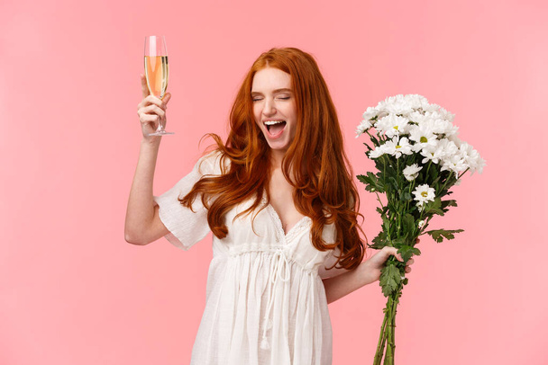 Podekscytowany i beztroski przystojny ruda kobieta świętuje wieczór panieński, krzyczeć tak z zamkniętymi oczami i zrelaksowany wyraz twarzy, uczucie niesamowite, trzymając kwiaty bukiet i podnieść szampana - Zdjęcie, obraz