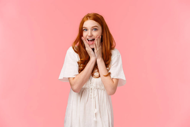 Expectation, anticipation and happiness concept. Amused cute redhead silly girl looking surprised and excited, gasping fascinated, looking charmed and amazed camera, pink background - Photo, Image