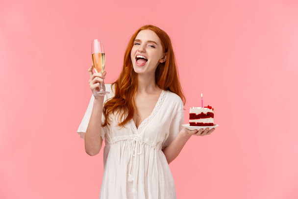 Waist-up portrait happy and excited chanting happy birthday song, raising glass champagne in cheers gesture, yelling amused, holding peace of b-day cake, having fun celebrating over pink background - Photo, Image