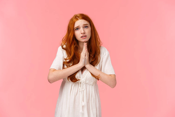 Pleading cute and silly redhead girl acting innocent, press hands together in pray, asking for favour, hopefully looking at camera, frowning gloomy, need something, begging over pink background - Photo, Image
