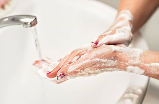 Young woman wash her hands under water tap faucet with soap. Detail on suds covered skin. Personal hygiene concept - coronavirus covid 19 outbreak prevention - Zdjęcie, obraz