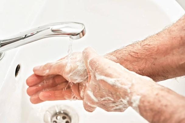 Senior elderly man his hands with soap under tap water faucet, detail photo. Can be used as hygiene illustration concept during coronavirus / covid19 outbreak prevention - Фото, зображення