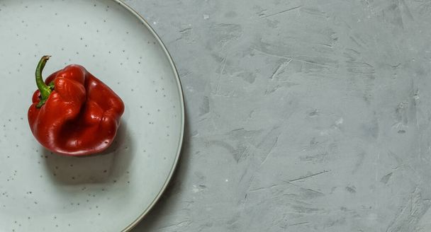  pimiento rojo feo en un plato, sobre un fondo gris áspero. Orientación horizontal con espacio, superior - Foto, Imagen