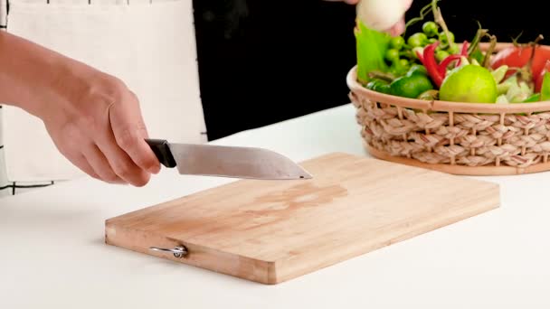 Vrouw snijdt verse groene Thaise aubergine in stukken met mes op houten snijplank. - Video