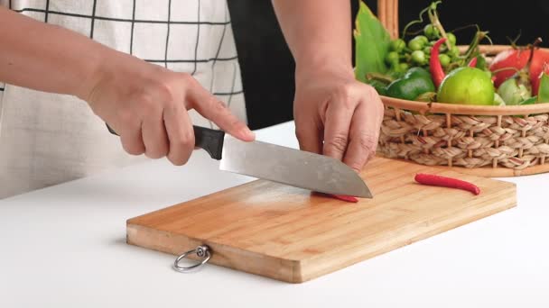 Vrouw snijdt verse rode chili in stukken met mes op houten snijplank. - Video