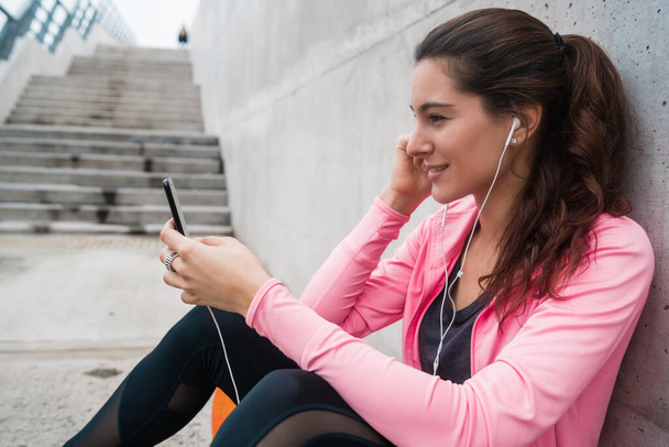 Portrait of an athletic woman using her mobile phone on a break from training against grey background. Sport and health lifestyle. - Foto, Imagen