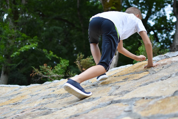 boy child climbs a stone mountain, conquering a high peak. - Fotoğraf, Görsel